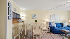 Ein gemütliches Wohnzimmer mit einem blauen Sofa, einem runden Esstisch mit Stühlen und einer Küchenzeile mit Holzschränken und einer Lampe.