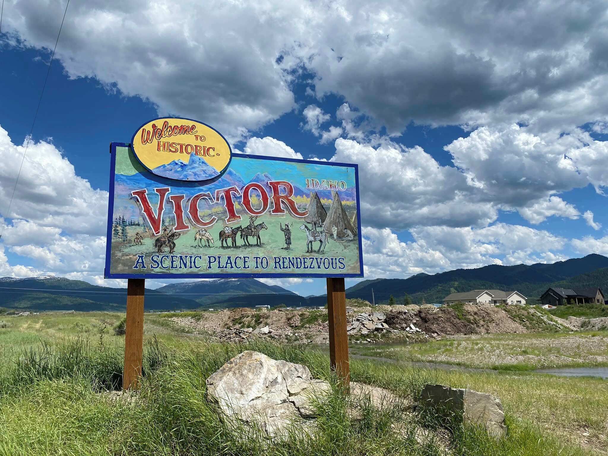 Letrero de bienvenida a Victor, Idaho, con un paisaje pintoresco al fondo.