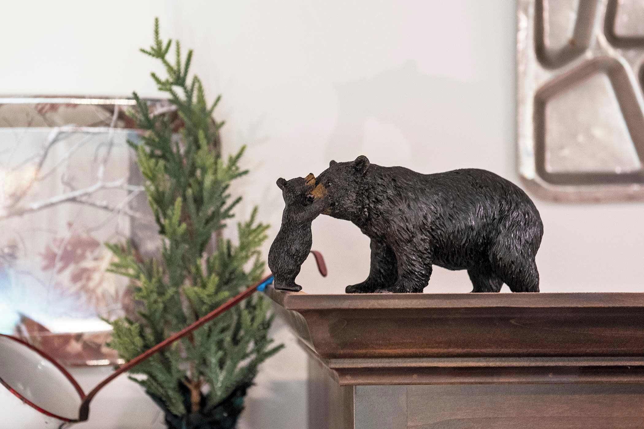 Une figurine d’ours posée sur une surface en bois, avec une plante en pot et un tableau encadré en arrière-plan.