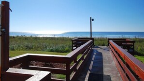 Une promenade en bois menant à l’accès à la plage, avec des tables de pique-nique et un lampadaire.