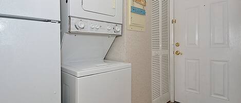 A laundry area with a washing machine and dryer, a welcome sign, and a door with a beach-themed mat.