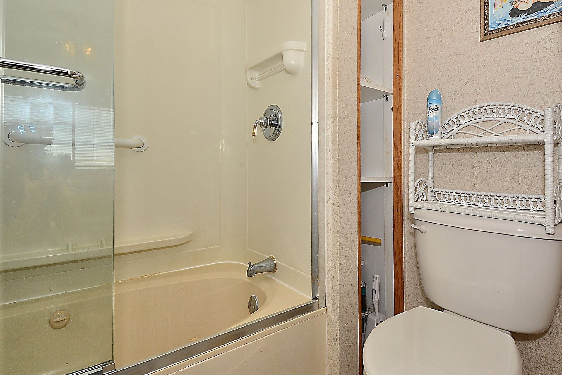 A bathroom with a glass-enclosed shower, a white toilet, and a decorative shelf with toiletries.