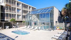 Un espace piscine doté de chaises longues et d’une piscine fermée par des parois en verre.