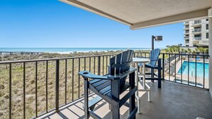 Ein Balkon mit zwei Adirondack-Stühlen, einem kleinen Tisch und Blick auf den Strand und den Ozean.