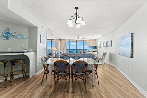 A dining area with a glass table, wicker chairs, and a view of the ocean through large windows.