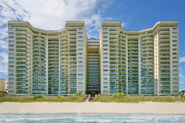 A high-rise hotel with multiple balconies, located adjacent to a beach.