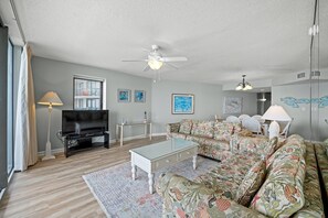 A living room with a sofa, coffee table, TV, ceiling fan, and artwork on the walls.