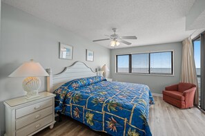 A bedroom with a bed, a nightstand, a lamp, a chair, a ceiling fan, and a window with blinds.