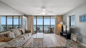 Ein geräumiges Wohnzimmer mit einer großen Sofagarnitur, einem Couchtisch und einem Fernseher. Das Zimmer verfügt über einen Balkon mit Meerblick.