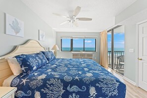 A bedroom with a bed, a ceiling fan, a window with a view of the ocean, and a door leading to a balcony.