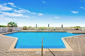 A swimming pool with a white fence, lounge chairs, and a clear blue sky. - 4-bedroom, 3-bathroom, oceanfront unit, sleeps 10 | Ocean Bay Club - 401 (North Myrtle Beach)
