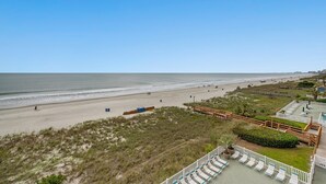 Blick auf einen Strand mit einer Holzterrasse und Liegestühlen.