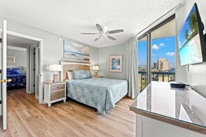 A hotel room with a bed, bedside tables, a ceiling fan, a large window with a view, and a TV mounted on the wall. - 4-bedroom, 3-bathroom, oceanfront unit, sleeps 10 | Ocean Bay Club - 401 (North Myrtle Beach)