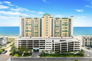 A multi-story hotel with a central courtyard, parking garage, and a view of the ocean. - 4-bedroom, 3-bathroom oceanfront condo with spacious private balcony - | Ocean Bay Club - 402 (North Myrtle Beach)
