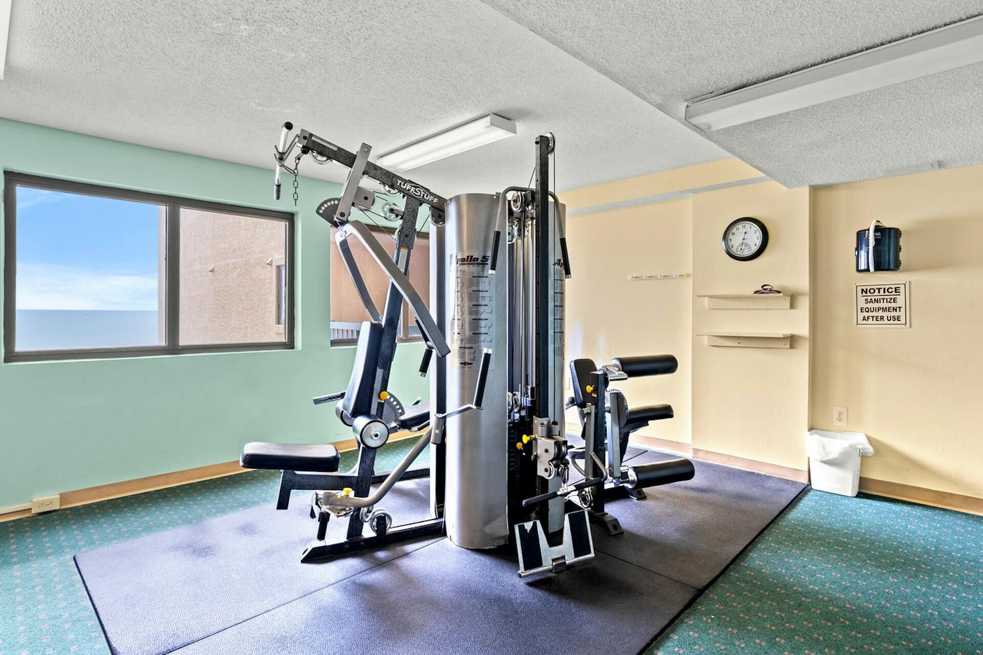 Ein Fitnessstudio mit Krafttrainingsgeräten, einer Uhr und einem Aushang an der Wand.