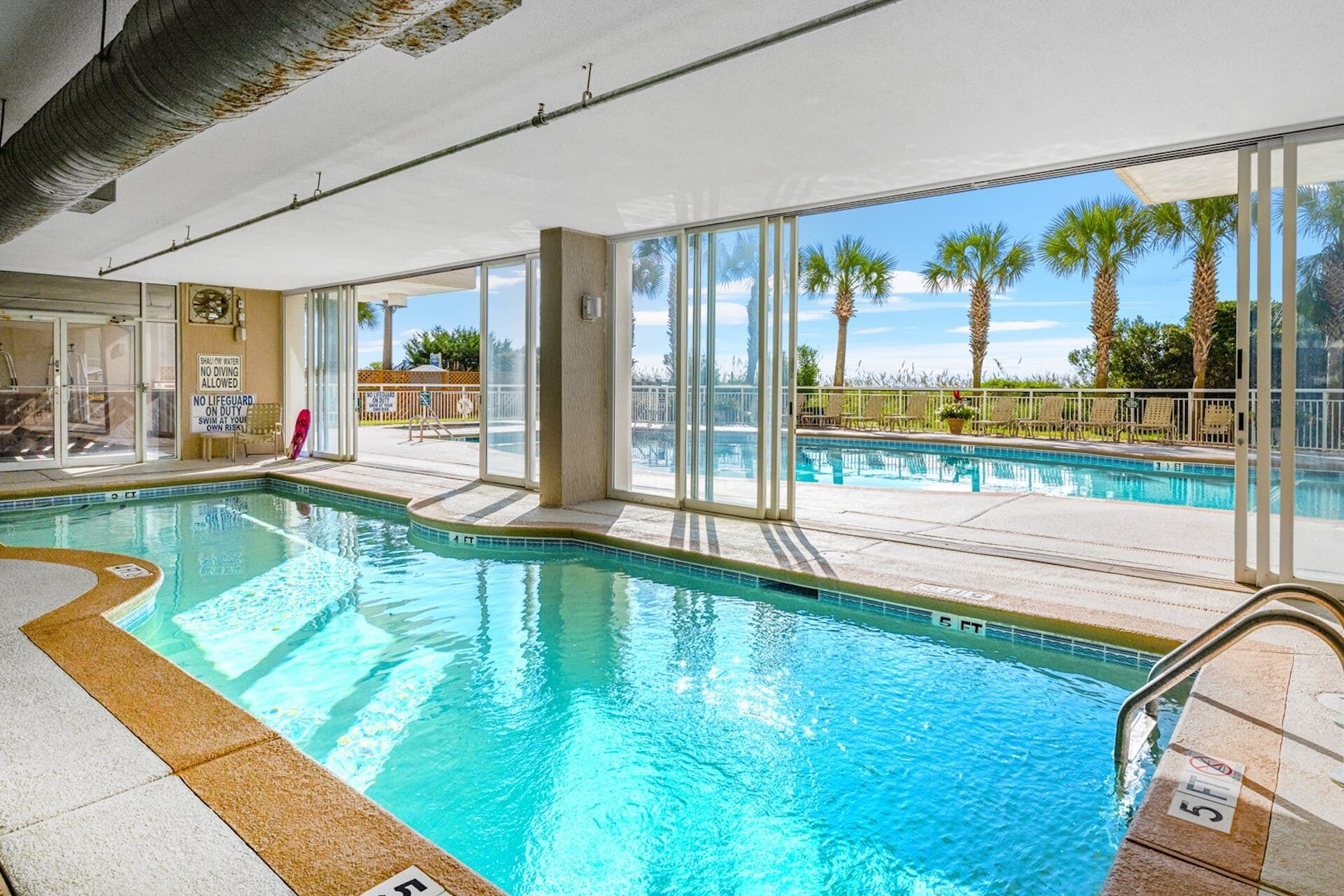 An indoor swimming pool with clear glass walls, a lifeguard chair, and a sign indicating no diving allowed.