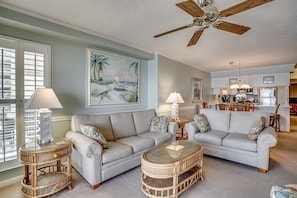 A living room with two sofas, a glass coffee table, and a ceiling fan. - Upscale 3-bed, 3-bath, 3rd floor oceanfront condo | Tidemaster - 302 (North Myrtle Beach)