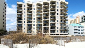 A multi-story residential building with balconies, a sandy ground level, and a clear sky. - Upscale 3-bed, 3-bath, 3rd floor oceanfront condo | Tidemaster - 302 (North Myrtle Beach)
