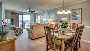 A spacious living room with a large sofa, a dining table with wicker chairs, and a ceiling fan. - Upscale 3-bed, 3-bath, 3rd floor oceanfront condo | Tidemaster - 302 (North Myrtle Beach)