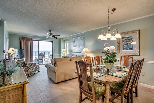 A spacious living room with a large sofa, a dining table with wicker chairs, and a ceiling fan.