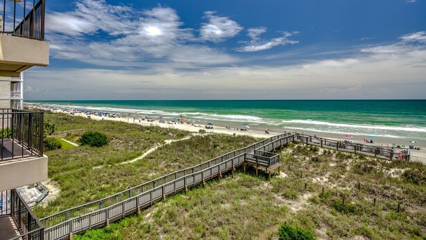 A beach view with a wooden boardwalk leading to the shore, a clear sky, and the ocean. - Upscale 3-bed, 3-bath, 3rd floor oceanfront condo | Tidemaster - 302 (North Myrtle Beach)