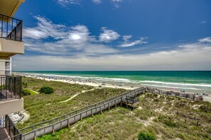 A beach view with a wooden boardwalk leading to the shore, a clear sky, and the ocean.