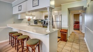 A modern kitchen with a central island, bar stools, and a view into a bedroom. - Upscale 3-bed, 3-bath, 3rd floor oceanfront condo | Tidemaster - 302 (North Myrtle Beach)