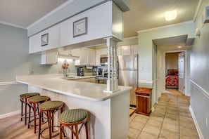 Cozinha moderna com ilha central, banquetas e vista para um quarto.