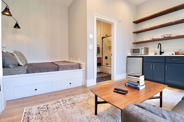 A modern living room with a built-in seating area, a coffee table, and a kitchen area with wooden shelves. - The Duke Suite at Prince Street Inn (Alexandria)