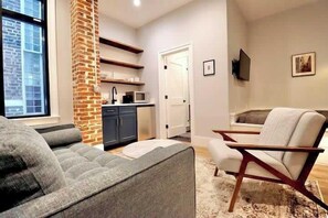 A living room with a sofa, a chair, a fireplace, a kitchen area, and a television.