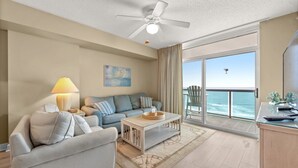 A spacious living room with a sofa, a coffee table, and a view of the ocean through a sliding glass door.