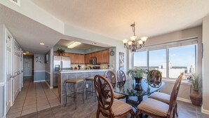 A spacious kitchen with wooden cabinets, a stainless steel refrigerator, and a large window offering a city view. - Stylish 4-bedroom condo with jetted tub and two king bedrooms | Crescent Shores - N 1101 (North Myrtle Beach)