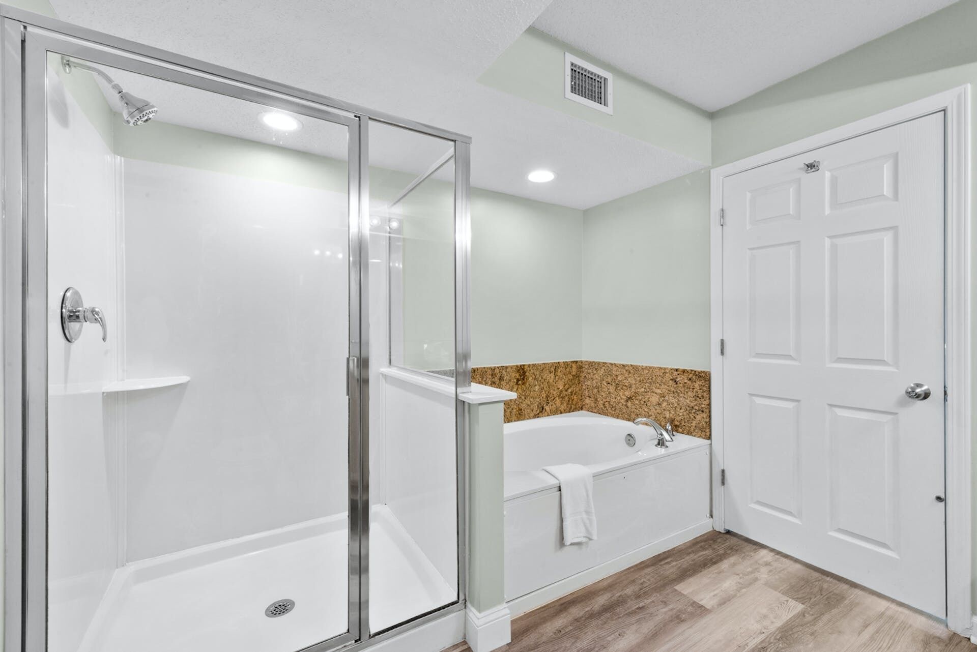 A bathroom with a glass-enclosed shower, a bathtub, and a white door.