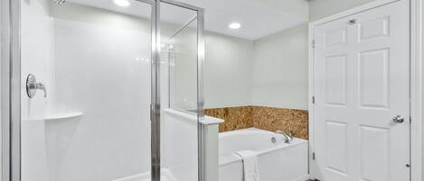 A bathroom with a glass-enclosed shower, a bathtub, and a white door.