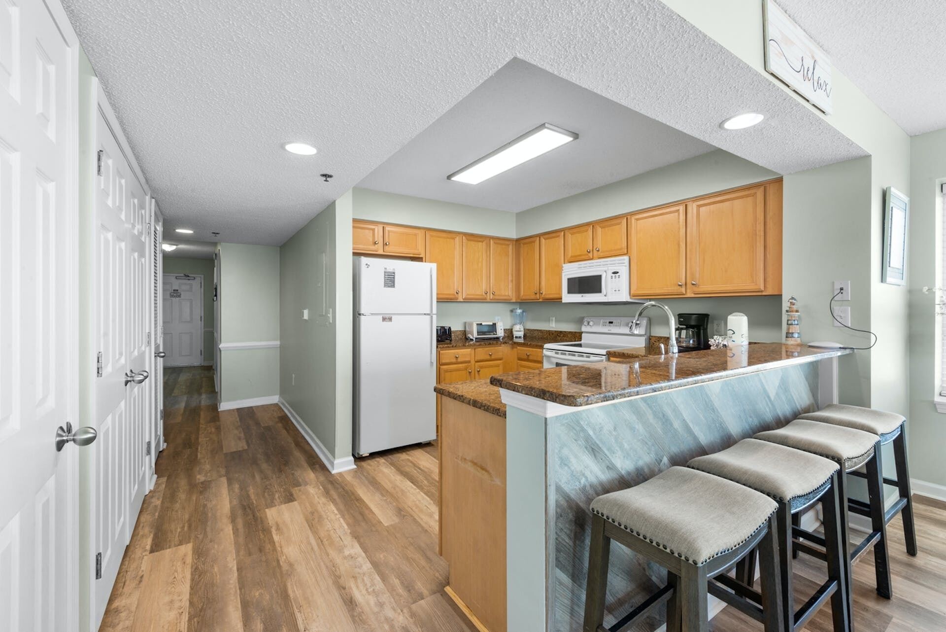 Una cocina moderna con armarios de madera, una isla central con taburetes de bar y un refrigerador.