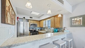 A modern kitchen with a granite countertop, stainless steel appliances, wooden cabinets, and pendant lighting. - Well designed 6th floor, 3-bedroom, 3-bath oceanfront condo | Crescent Tower 1 - 601 (North Myrtle Beach)