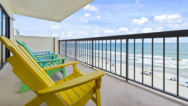 A balcony with yellow and green Adirondack chairs overlooking a beach with people and umbrellas. - Well designed 6th floor, 3-bedroom, 3-bath oceanfront condo | Crescent Tower 1 - 601 (North Myrtle Beach)