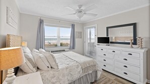 Een slaapkamer met een bed, een dressoir, een televisie en een plafondventilator.