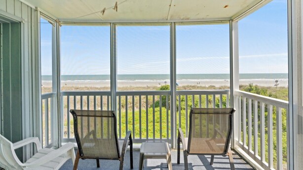 Een overdekte veranda met twee stoelen en een kleine tafel, met uitzicht op een strand.