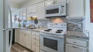 A kitchen with white cabinets, a double oven, a microwave, and a granite countertop. - Classic beachfront condo with two beds and two baths, private balcony | Crescent Sands - 3-B (North Myrtle Beach)
