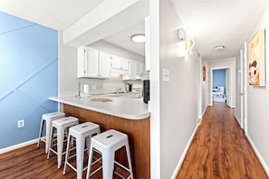 A modern kitchen with white cabinets, a bar area with stools, and a wooden floor. - Cool condo with unique design, 3 bedrooms | Crescent Sands - 5-F (North Myrtle Beach)