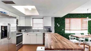 A modern kitchen with white cabinets, a wooden dining table, and a green wall accent. - Manatee Pocket! Whole House & Backyard to Yourself (Stuart)