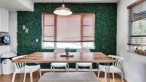 A dining area with a wooden table, white chairs, a hanging light fixture, and a window with blinds. - Manatee Pocket! Whole House & Backyard to Yourself (Stuart)