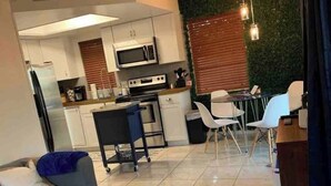 A modern living room with a sofa, a bench, and a dining area with a table and chairs. There is a kitchen in the background with a microwave, stove, and cabinets. - Manatee Pocket! Whole House & Backyard to Yourself (Stuart)