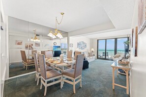 A spacious room with a dining area, a sofa, and a large window with a view. - 3-bedroom oceanfront condo with private balcony | Crescent Sands - 5-G (North Myrtle Beach)