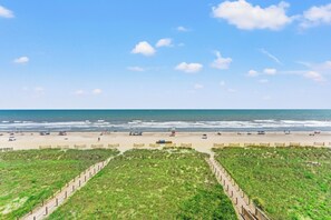 A beach with a clear sky, sandy shore, and a grassy area with a fence. - 3-bedroom oceanfront condo with private balcony | Crescent Sands - 5-G (North Myrtle Beach)