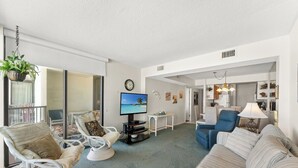 Ein Wohnzimmer mit Fernseher, Sitzgelegenheiten und einem Balkon.