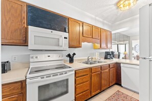 A kitchen with wooden cabinets, a microwave, stove, and a dishwasher. - 3-bedroom oceanfront condo with private balcony | Crescent Sands - 5-G (North Myrtle Beach)