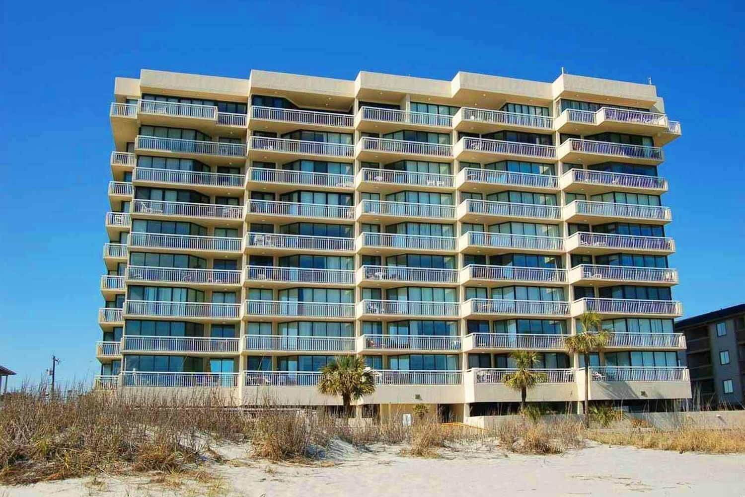 Een meerhoog hotel met balkons op elke verdieping, nabij een strand.