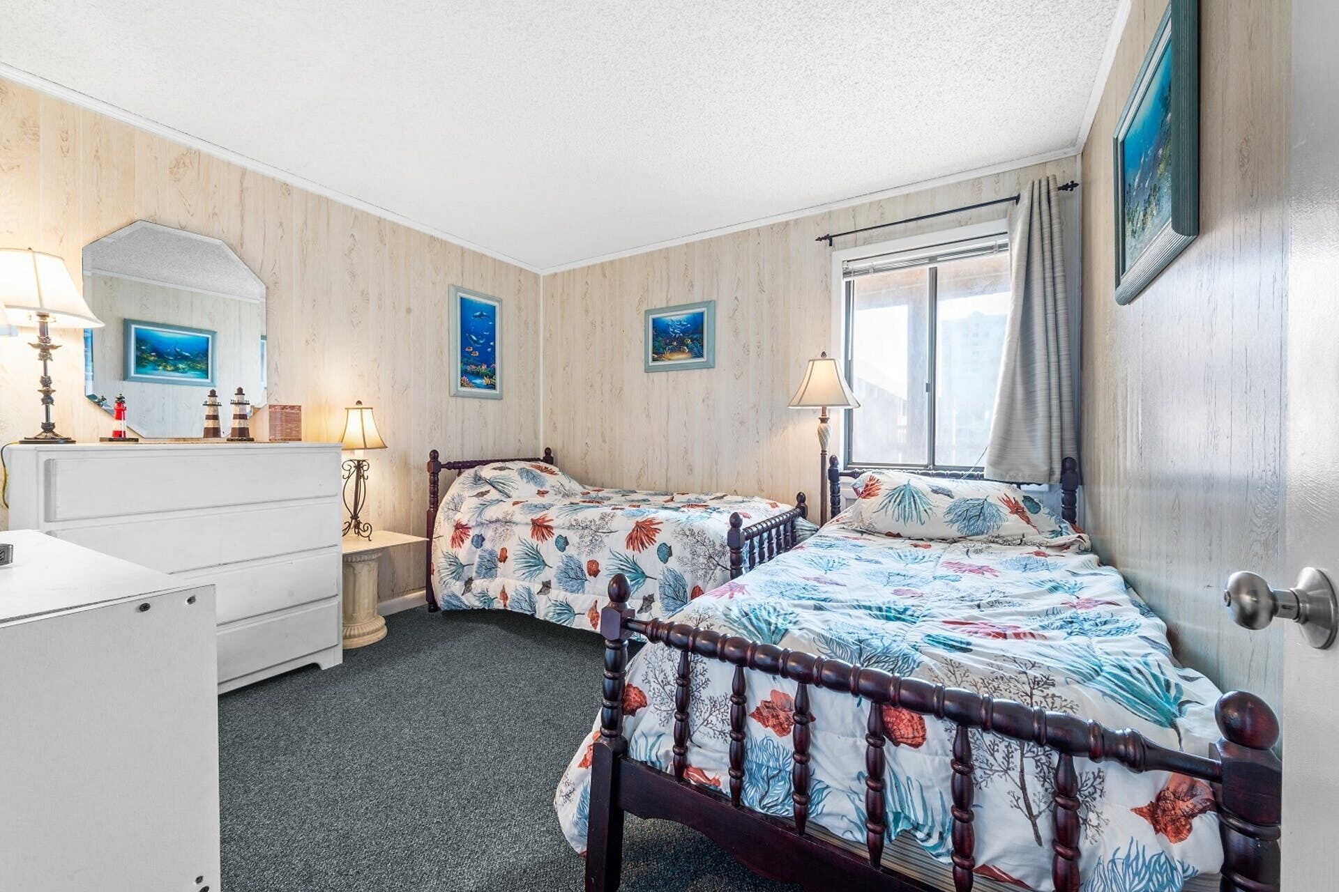 A bedroom with two beds, a dresser, a window with curtains, and two wall-mounted paintings.